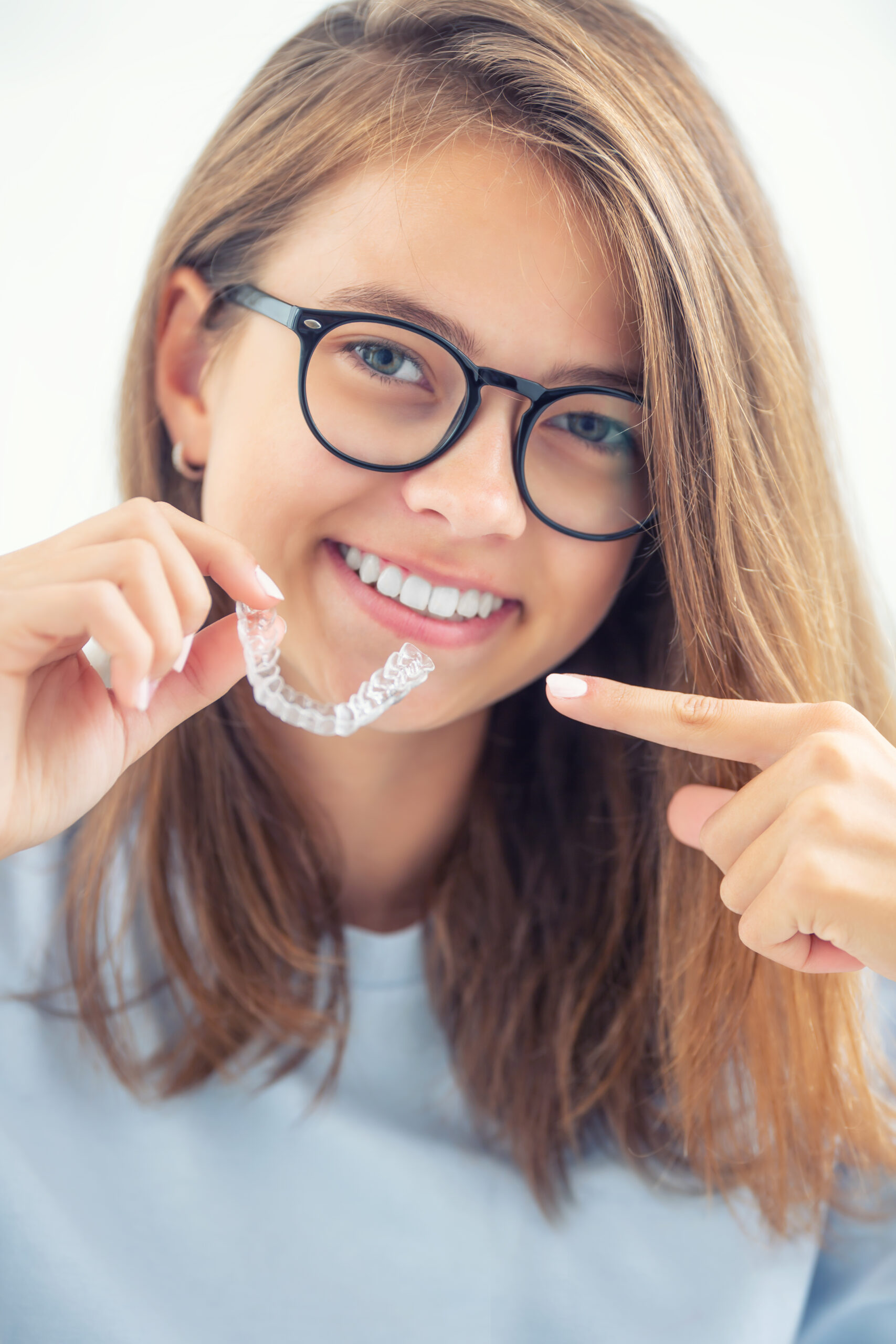 Mulher sorrindo aponta para os dentes com alinhador transparente