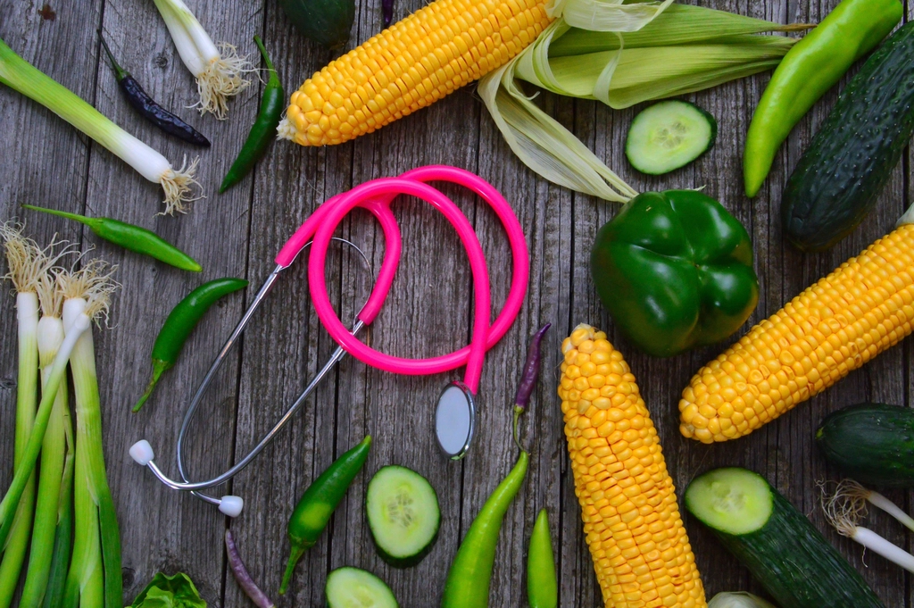 Legumes e verduras ao redor de um estetoscópio sobre mesa de madeira